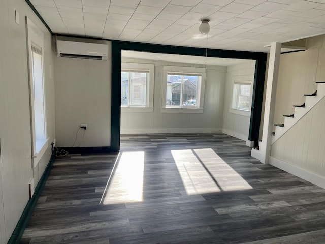 spare room featuring dark wood-type flooring, an AC wall unit, stairs, and baseboards