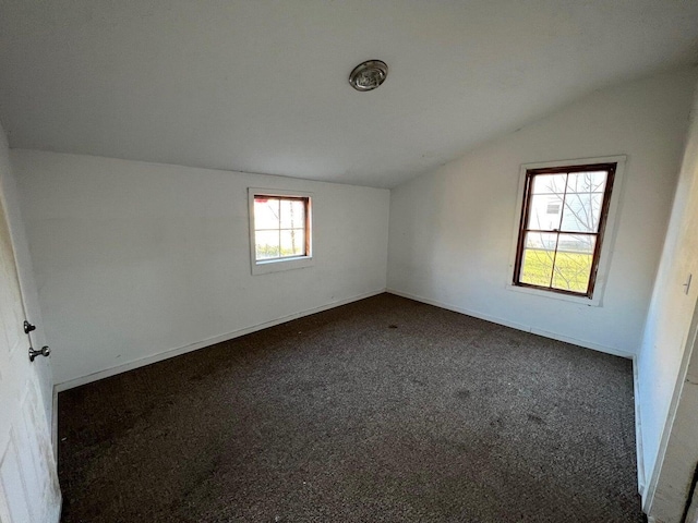 empty room featuring dark carpet, baseboards, and lofted ceiling