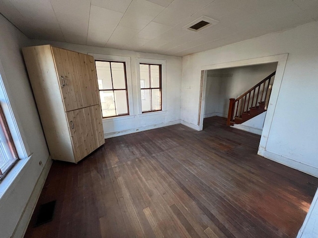 unfurnished room featuring baseboards, dark wood-style flooring, stairs, and visible vents