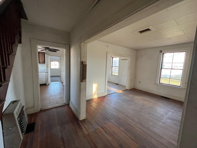 empty room with baseboards, visible vents, dark wood finished floors, and a wealth of natural light