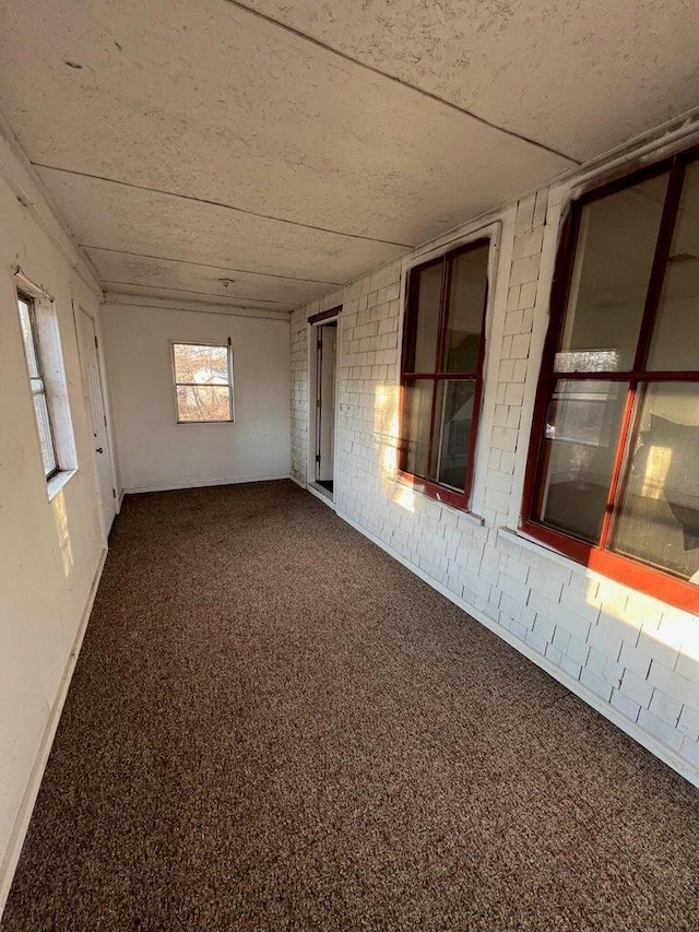 spare room with baseboards, a drop ceiling, and dark colored carpet