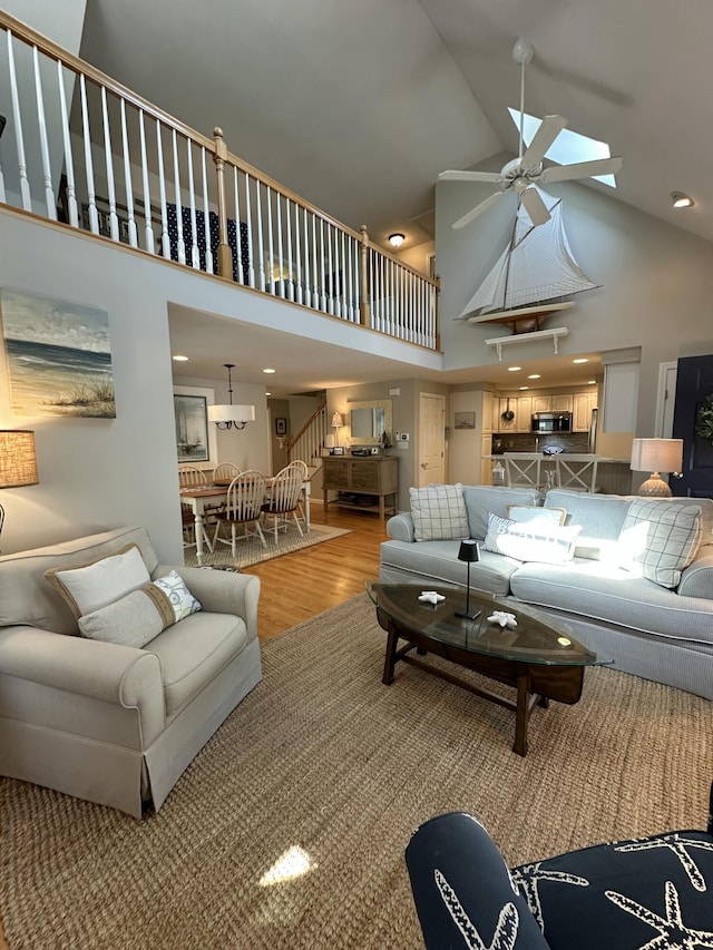 living area with light wood-style floors, stairs, ceiling fan, and high vaulted ceiling