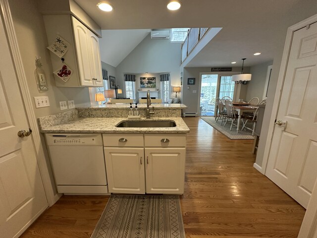 kitchen with a peninsula, white dishwasher, a wall mounted AC, white cabinets, and a sink