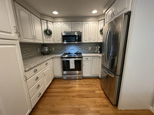 kitchen with light stone countertops, stainless steel appliances, light wood finished floors, and white cabinetry