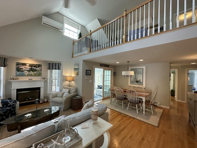 living area with wood finished floors, a fireplace, baseboard heating, high vaulted ceiling, and an AC wall unit