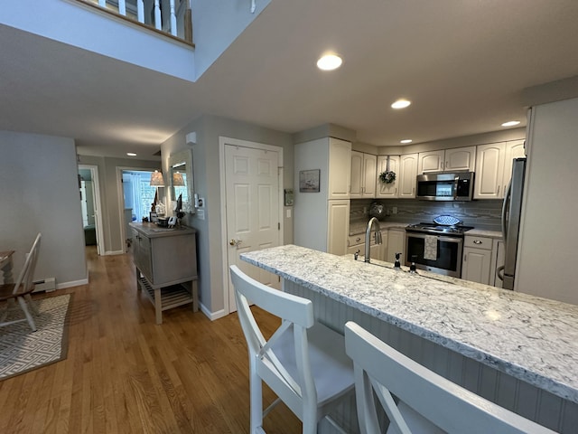 kitchen with wood finished floors, baseboards, a kitchen bar, a sink, and appliances with stainless steel finishes