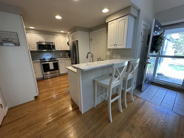 kitchen featuring white cabinets, appliances with stainless steel finishes, a sink, light wood-style flooring, and a peninsula