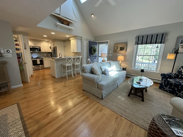 living area with light wood-style floors, high vaulted ceiling, recessed lighting, a baseboard heating unit, and a skylight
