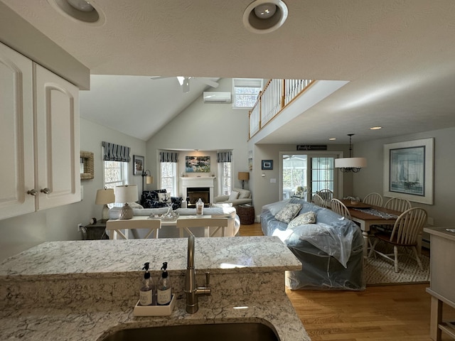 kitchen with a sink, light wood finished floors, a fireplace, a ceiling fan, and a wall mounted AC