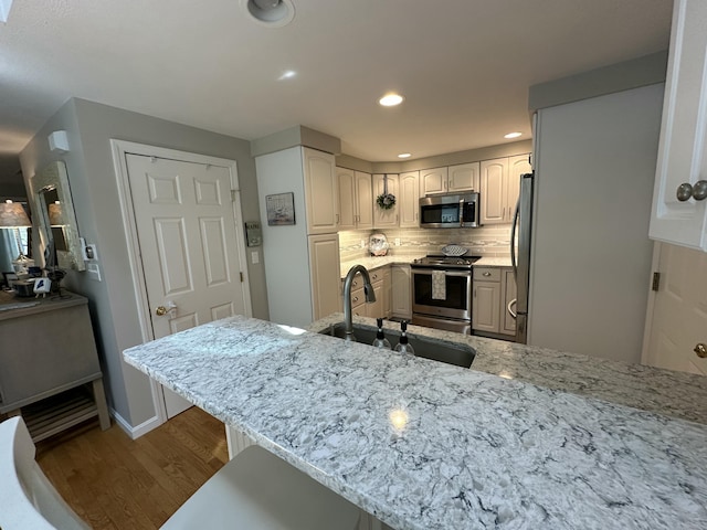 kitchen with decorative backsplash, wood finished floors, light stone counters, a sink, and appliances with stainless steel finishes