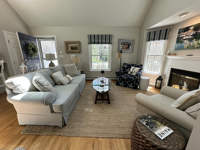 living room featuring a glass covered fireplace, vaulted ceiling, and wood finished floors