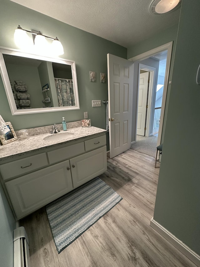 bathroom featuring a textured ceiling, a baseboard heating unit, wood finished floors, and vanity