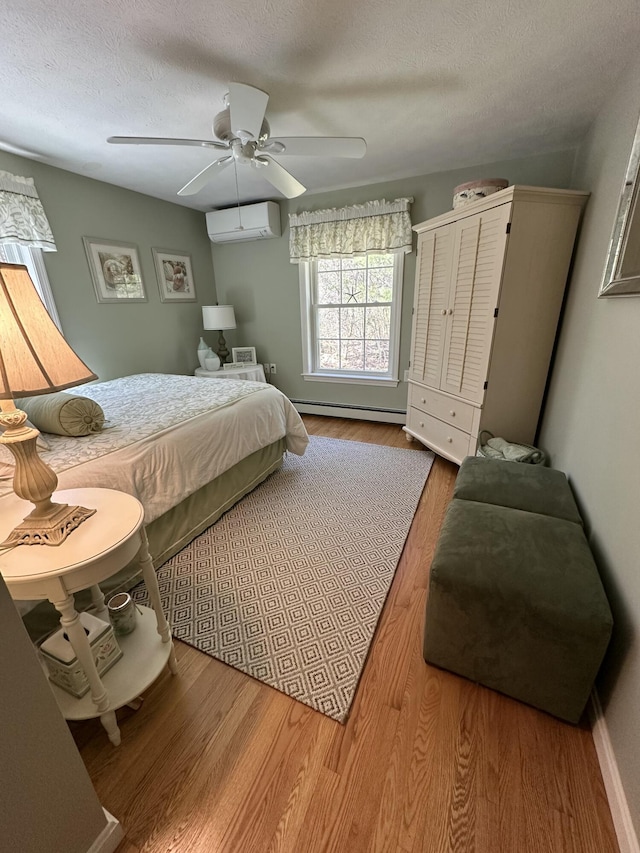 bedroom with wood finished floors, ceiling fan, a textured ceiling, a baseboard heating unit, and a wall mounted AC
