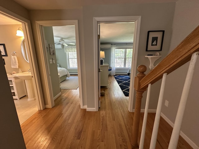 hallway with baseboards, an AC wall unit, and light wood finished floors