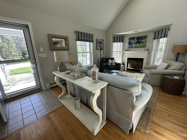 living room with a glass covered fireplace, a baseboard heating unit, light tile patterned flooring, and high vaulted ceiling