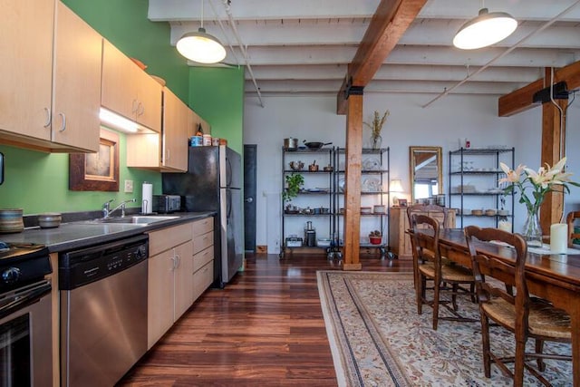 kitchen with a sink, beamed ceiling, dark countertops, appliances with stainless steel finishes, and dark wood-style floors
