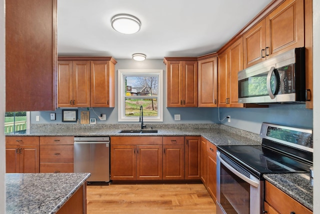 kitchen featuring light wood-type flooring, a sink, brown cabinetry, and appliances with stainless steel finishes