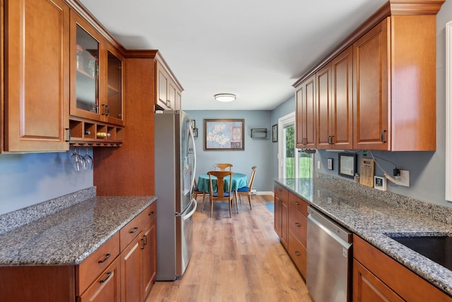 kitchen with stainless steel appliances, brown cabinetry, glass insert cabinets, and light wood-type flooring