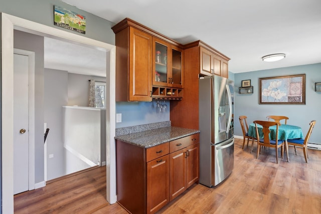 kitchen with stainless steel fridge, stone countertops, brown cabinetry, light wood-style flooring, and glass insert cabinets