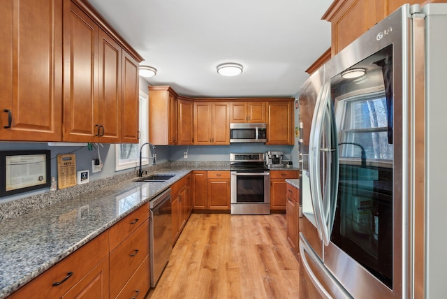 kitchen featuring brown cabinets, appliances with stainless steel finishes, a sink, a wealth of natural light, and light wood-type flooring
