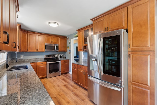 kitchen with a sink, appliances with stainless steel finishes, brown cabinetry, and light wood-type flooring