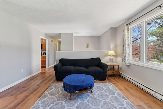 sitting room with a textured ceiling, baseboards, a baseboard heating unit, and wood finished floors