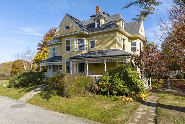 victorian-style house featuring a front lawn, covered porch, and a chimney
