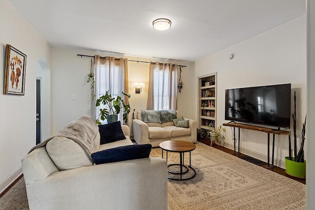 living room featuring built in shelves, baseboards, and wood finished floors