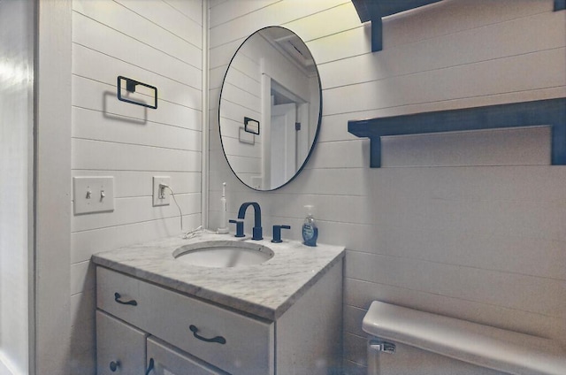bathroom featuring vanity, wood walls, and toilet