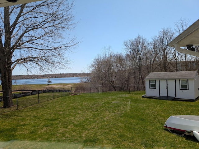 view of yard with an outdoor structure, a water view, fence, and a storage shed