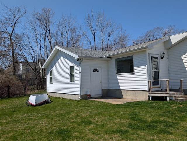 back of house featuring a lawn, fence, and roof with shingles