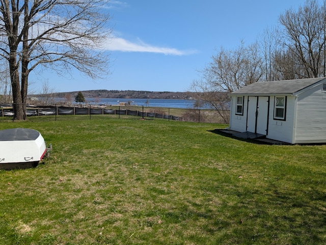 view of yard featuring a water view, fence, an outbuilding, and a storage unit