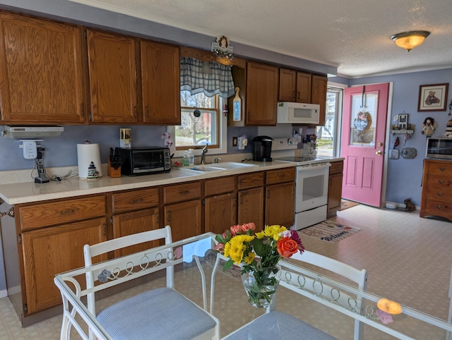 kitchen featuring white appliances, brown cabinetry, a sink, and light floors