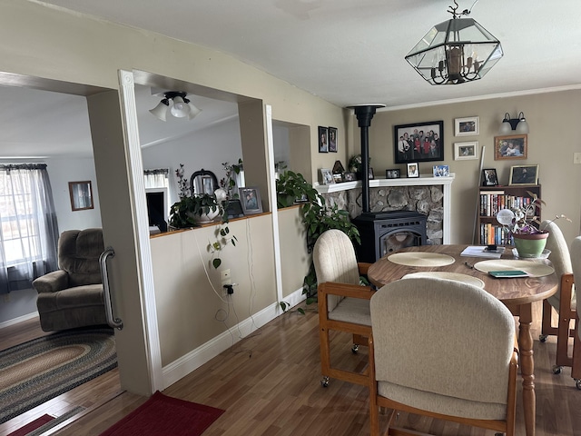 dining area featuring a ceiling fan, baseboards, wood finished floors, and a wood stove