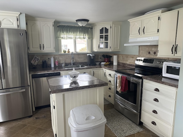 kitchen with a sink, appliances with stainless steel finishes, under cabinet range hood, and dark countertops
