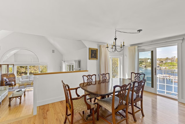 dining space with light wood-style flooring, a notable chandelier, a healthy amount of sunlight, and vaulted ceiling