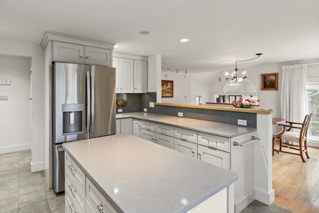 kitchen with a center island, tasteful backsplash, stainless steel fridge with ice dispenser, baseboards, and a peninsula
