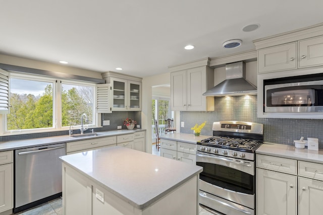 kitchen featuring wall chimney range hood, decorative backsplash, a kitchen island, a sink, and stainless steel appliances