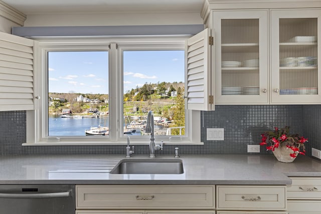 kitchen featuring white cabinets, a sink, tasteful backsplash, stainless steel dishwasher, and glass insert cabinets