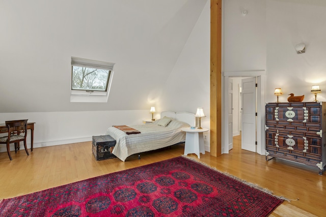bedroom featuring baseboards, lofted ceiling with skylight, and wood finished floors