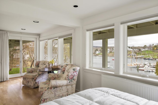sunroom featuring radiator, a water view, and wood finished floors
