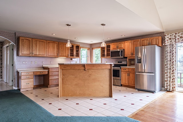kitchen with decorative light fixtures, appliances with stainless steel finishes, brown cabinetry, and glass insert cabinets
