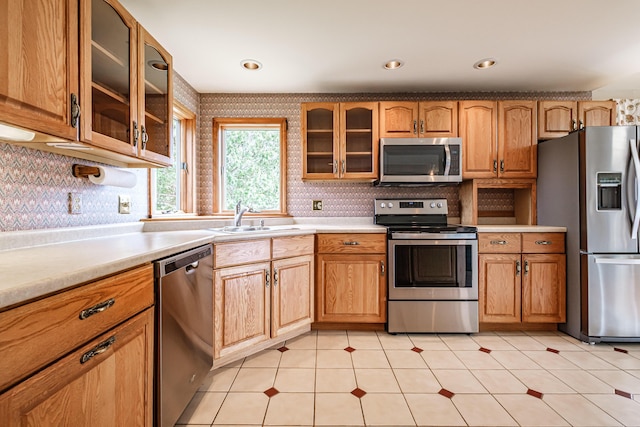 kitchen featuring a sink, appliances with stainless steel finishes, glass insert cabinets, and light countertops