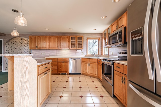 kitchen featuring pendant lighting, appliances with stainless steel finishes, a sink, light countertops, and glass insert cabinets