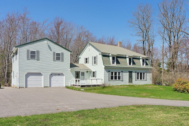 colonial inspired home featuring driveway, metal roof, a chimney, a front yard, and a garage