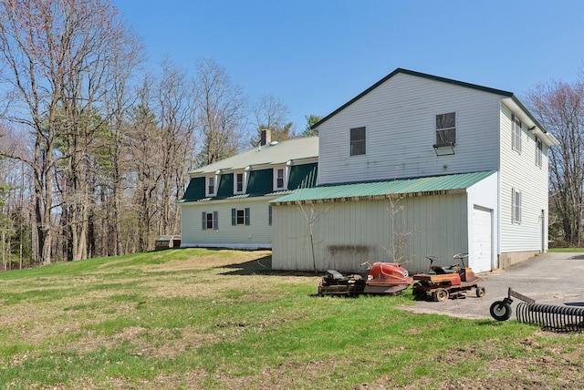 rear view of property with a lawn, an attached garage, metal roof, and a chimney