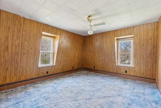 carpeted empty room with wooden walls, a ceiling fan, and a wealth of natural light