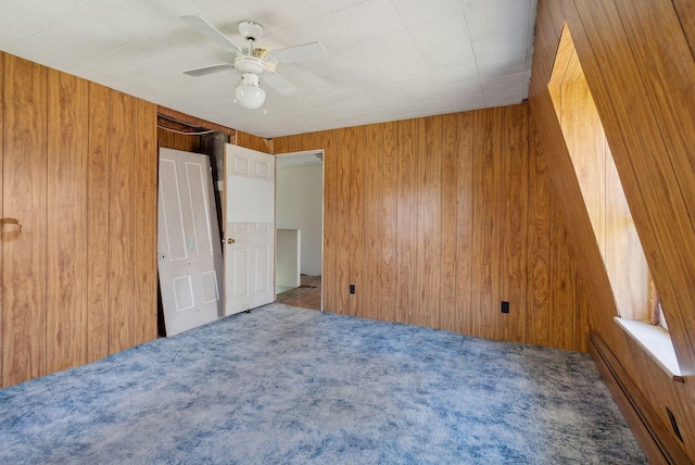unfurnished bedroom with wooden walls, a baseboard radiator, carpet flooring, and ceiling fan