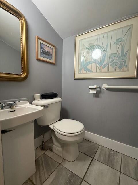 half bath with baseboards, vaulted ceiling, and toilet