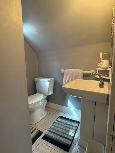 half bathroom with toilet, baseboards, and lofted ceiling
